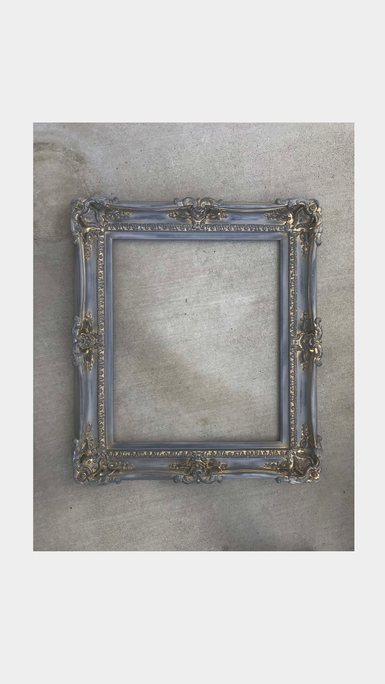 Puede incluir: Un marco de imagen ornamentado en gris y dorado con un dise&ntilde;o decorativo y detallado. El marco est&aacute; hecho de madera y tiene un acabado desgastado.
