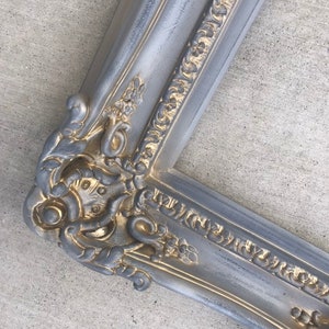 Puede incluir: Un marco de imagen ornamentado en plata y oro con un dise&ntilde;o detallado e intrincado. El marco tiene un aspecto desgastado y antiguo.