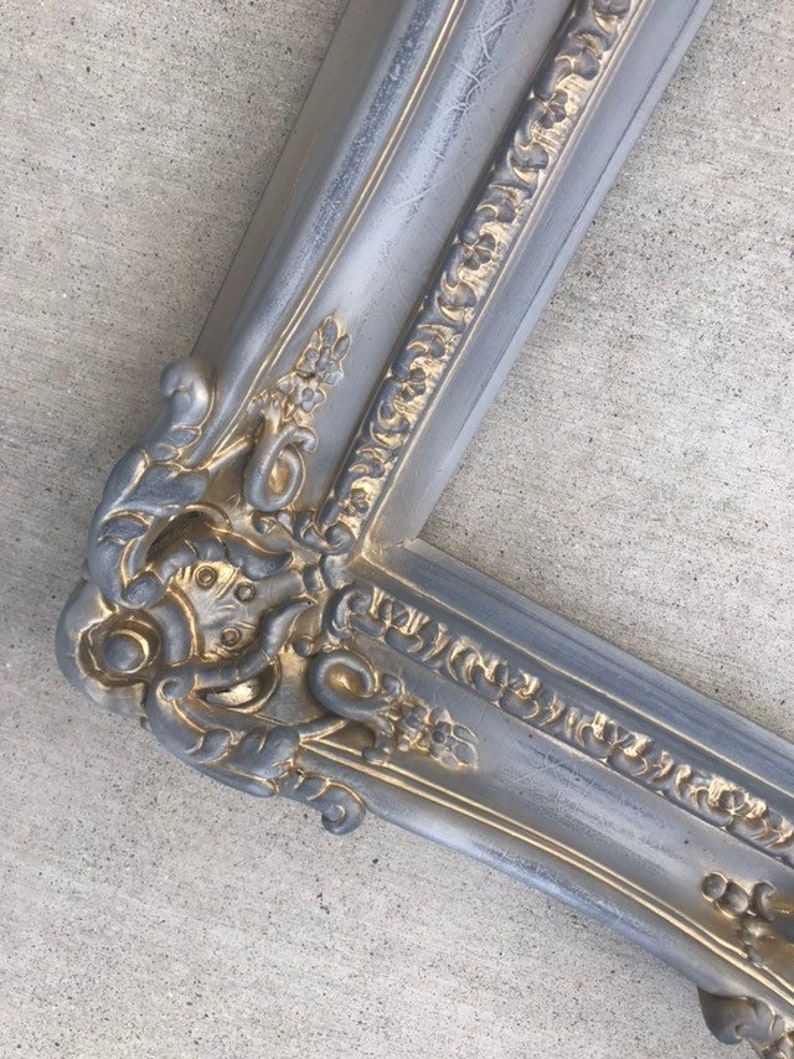 Puede incluir: Un marco de imagen ornamentado en plata y oro con un dise&ntilde;o detallado e intrincado. El marco tiene un aspecto desgastado y antiguo.