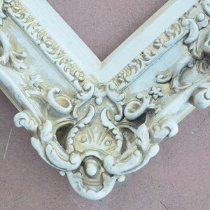 May include: A white ornate picture frame with a gold-toned design. The frame has a decorative, ornate design with a raised, textured surface.