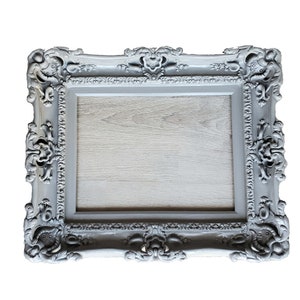 May include: A gray ornate picture frame with a wood-like surface inside. The frame has a detailed, decorative design.