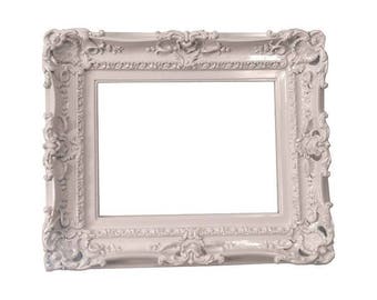 May include: A white ornate picture frame with a decorative, detailed design. The frame is made of a smooth, glossy material.