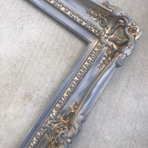 Puede incluir: Un marco de imagen adornado en plata y oro con un dise&ntilde;o detallado. El marco est&aacute; hecho de madera y tiene un acabado desgastado.