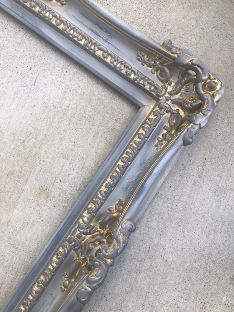 Puede incluir: Un marco de imagen adornado en plata y oro con un dise&ntilde;o detallado. El marco est&aacute; hecho de madera y tiene un acabado desgastado.