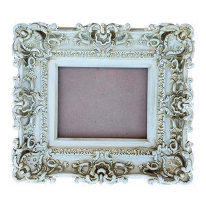 May include: An ornate white picture frame with a gold-toned finish. The frame has a detailed, intricate design with floral motifs and a raised edge.