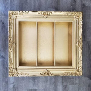 May include: A gold-colored picture frame with three compartments. The frame has a decorative, ornate design.
