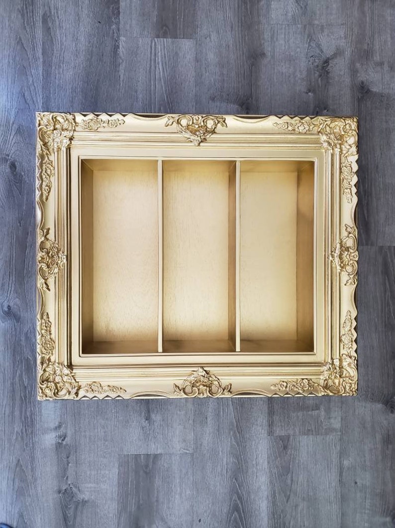 May include: A gold-colored picture frame with three compartments. The frame has a decorative, ornate design.