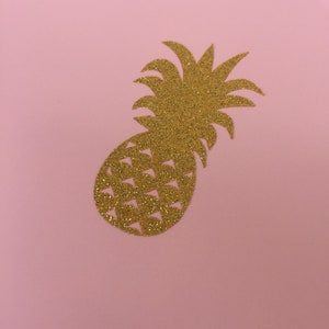May include: A gold glitter pineapple cutout on a pink background.