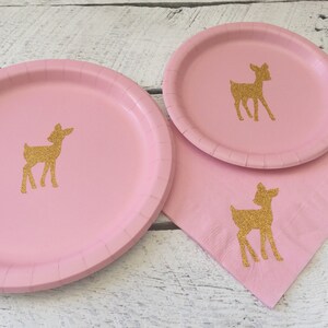 May include: Pink paper plates with gold glitter deer silhouettes. The plates are perfect for a woodland themed party.
