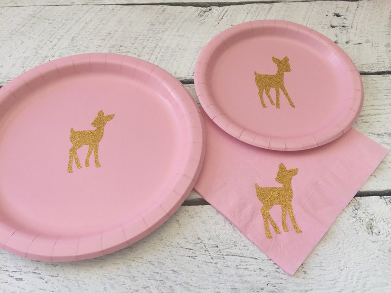 May include: Pink paper plates with gold glitter deer silhouettes. The plates are perfect for a woodland themed party.