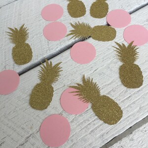 May include: Gold glitter pineapple and pink circle confetti. The confetti is scattered on a white wooden surface.