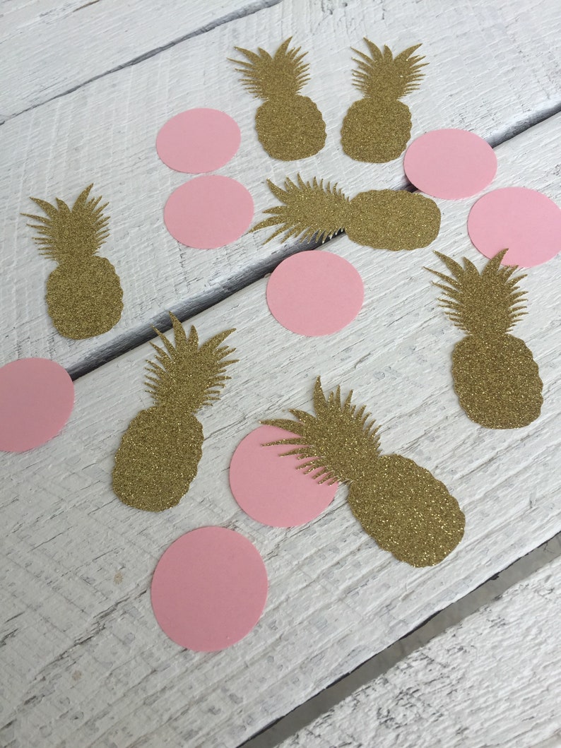 May include: Gold glitter pineapple and pink circle confetti. The confetti is scattered on a white wooden surface.