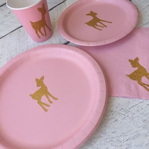 May include: Pink paper plates and cups with gold glitter deer silhouettes. The plates are 9 inches in diameter. The cups are 9 ounces.