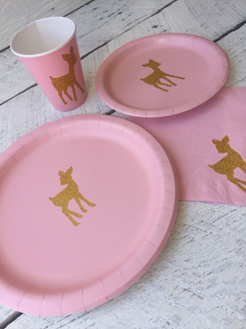 May include: Pink paper plates and cups with gold glitter deer silhouettes. The plates are 9 inches in diameter. The cups are 9 ounces.