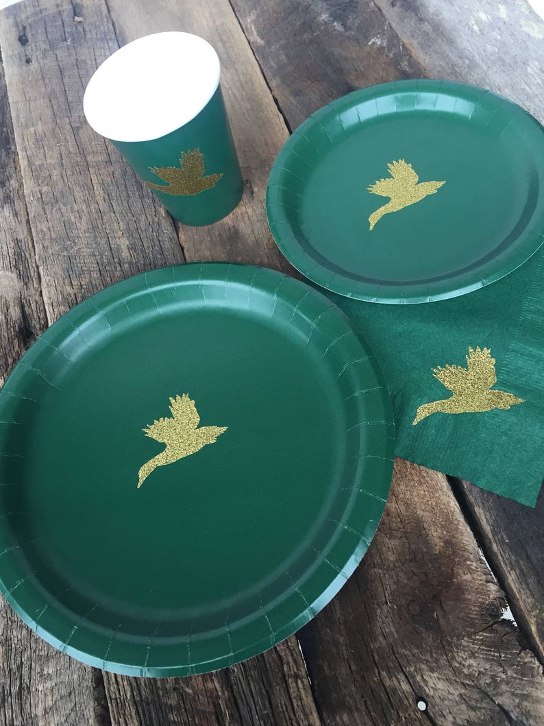 May include: Green paper plates and cups with gold glitter bird designs. The plates are round and have a scalloped edge. The cups are white with a green rim and bottom.
