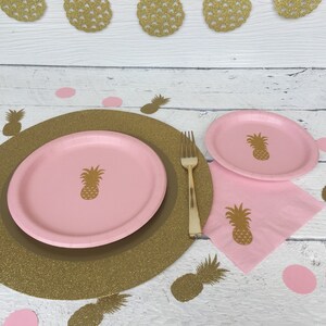 May include: A pink and gold pineapple themed table setting with a gold glitter charger, a pink dinner plate, a pink dessert plate, a pink napkin, and a gold fork. The table setting is decorated with pink and gold pineapple cutouts.