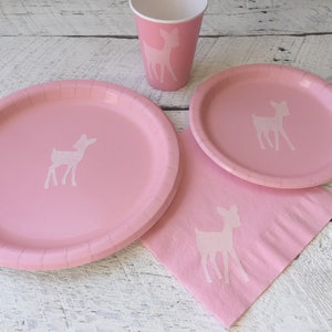 May include: Pink paper plates and cups with a white silhouette of a deer. Pink paper napkins with a white silhouette of a deer.