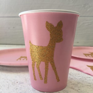 May include: Pink paper cup with a gold glitter deer silhouette. The cup is perfect for a party or special occasion.