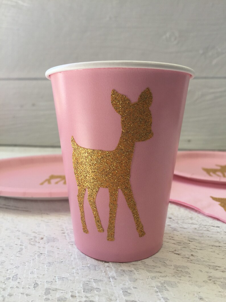 May include: Pink paper cup with a gold glitter deer silhouette. The cup is perfect for a party or special occasion.