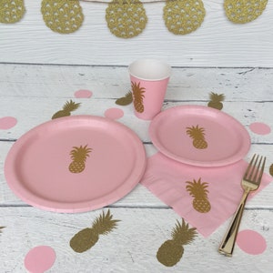 May include: Pink paper plates, cups, and napkins with a pineapple design. Gold glitter pineapple confetti is scattered on a white wooden surface.