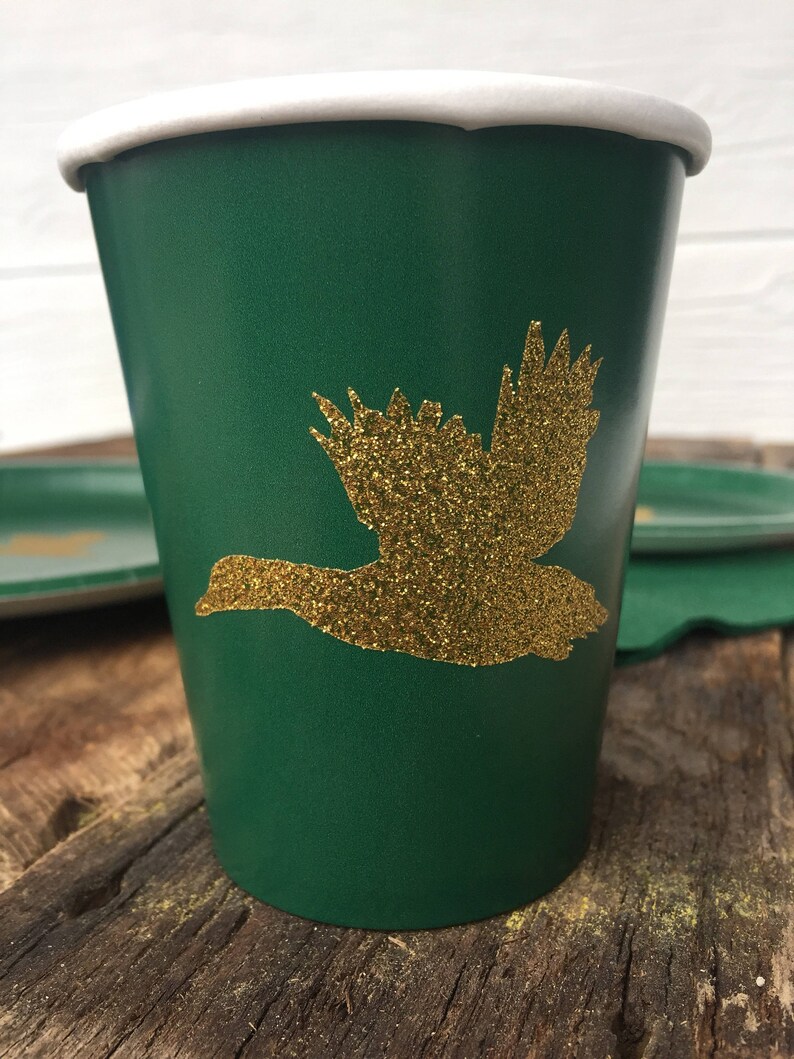 May include: A green paper cup with a gold glitter flying duck design. The cup has a white rim.