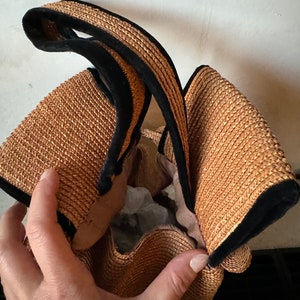 May include: A brown woven straw bag with black velvet trim. The bag has a single handle and is open at the top.