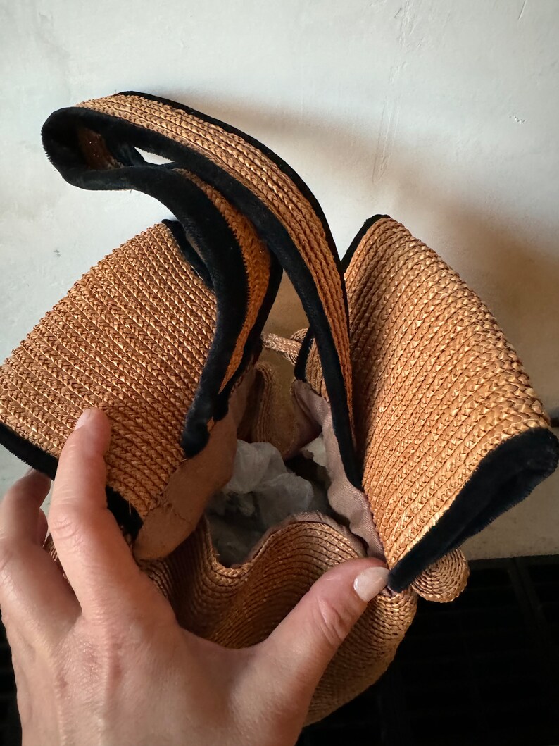 May include: A brown woven straw bag with black velvet trim. The bag has a single handle and is open at the top.