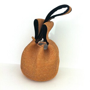 May include: A brown woven straw bag with black fabric handles. The bag is round and has a drawstring closure.