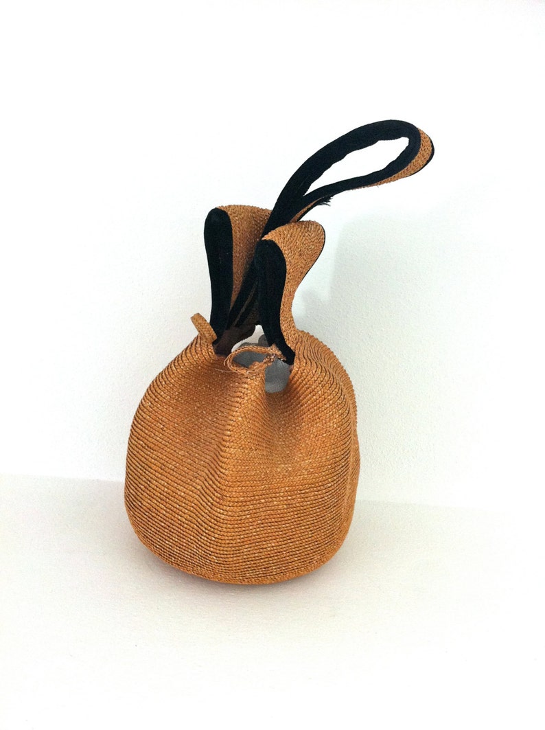 May include: A brown woven straw bag with black fabric handles. The bag is round and has a drawstring closure.