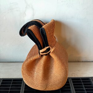 May include: A brown woven bag with black trim and a drawstring closure.