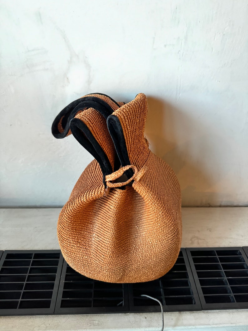 May include: A brown woven bag with black trim and a drawstring closure.