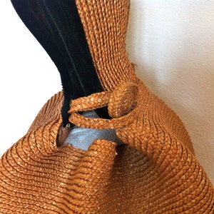 May include: A brown woven straw bag with a black velvet strap. The bag has a unique shape and a woven detail on the strap.