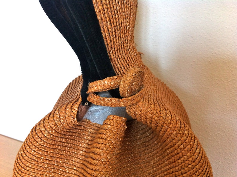 May include: A brown woven straw bag with a black velvet strap. The bag has a unique shape and a woven detail on the strap.