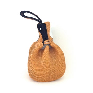 May include: A tan woven drawstring bag with black fabric handles. The bag is made of a textured material and has a round shape.