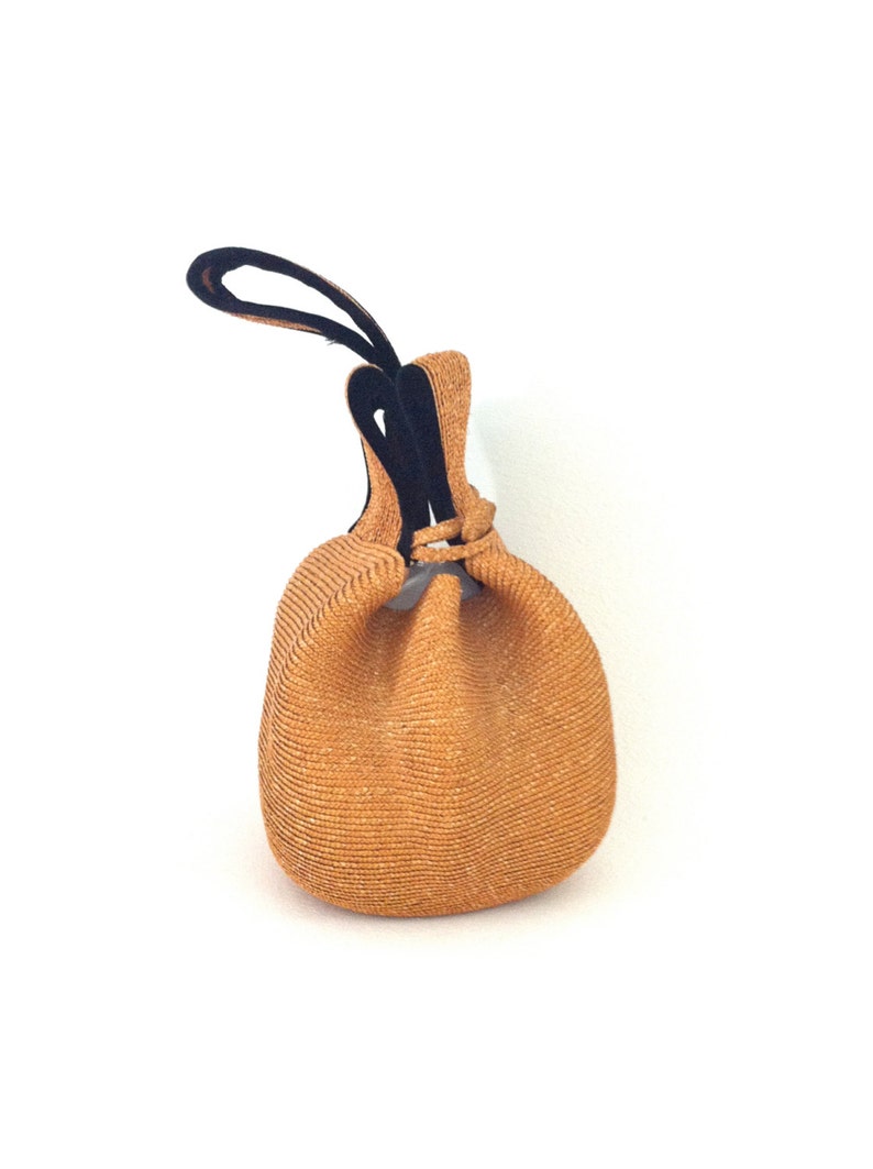 May include: A tan woven drawstring bag with black fabric handles. The bag is made of a textured material and has a round shape.