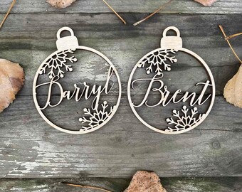 May include: Two wooden Christmas ornaments in the shape of a ball with snowflakes cut out. The ornaments are personalized with the names "Darryl" and "Brent".