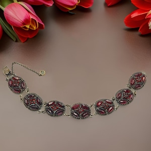 以下が含まれることがあります： チェーン留め具の赤いガーネットブレスレット。ブレスレットは、それぞれ赤いガーネットのクラスターがセットされた楕円形のリンクでできています。