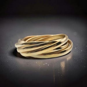 May include: A gold-toned multi-band ring featuring several interlocking, smooth, polished circular bands that overlap to create a single cohesive piece of jewelry with a continuous, rounded profile and a reflective metallic surface finish.