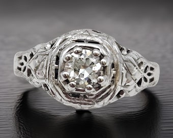 May include: A vintage silver ring with a delicate floral design and a single round diamond in the center.