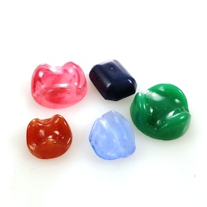 May include: Five different colored glass cabochons. The cabochons are in the shapes of a rectangle, a teardrop, and a rounded oval. The colors are pink, blue, green, red, and dark blue.