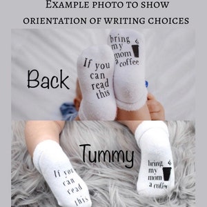 May include: A pair of white baby socks with black text that reads "If you can read this bring my mom a coffee". The socks are shown on a baby's feet in two different positions, one with the text facing the camera and the other with the text facing away from the camera.