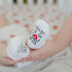 K&ouml;nnte beinhalten: Ein Paar wei&szlig;e Babyschuhe mit schwarzem Text. Ein Sch&uuml;hchen sagt "Nimm mich mit auf den Bauernhof!" mit einem roten Scheunen-Symbol. Das andere Sch&uuml;hchen sagt "Ich kann das lesen".