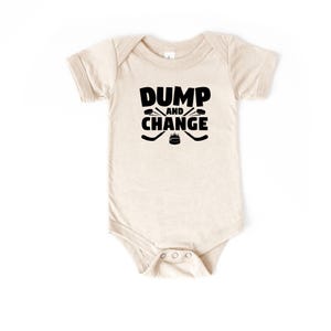 Może przedstawiać: Beżowe body dla dziecka z czarnym napisem "DUMP and CHANGE". Projekt zawiera skrzyżowane kije hokejowe i krążek. Ubranko ma krótkie rękawy i zatrzaski na dole ułatwiające przewijanie.