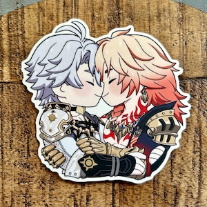 May include: A die-cut sticker featuring two anime-style characters with chibi proportions facing each other. One character has silver hair and white armor, while the other has blonde hair, red accents, and dark armor. Both wear intricate gold-toned gauntlets.