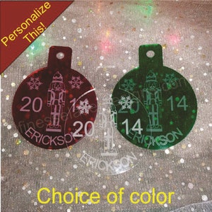 May include: Two round Christmas ornaments with a nutcracker design. The ornaments are made of clear acrylic with a red and green glitter finish. The ornaments are personalized with the year 2014 and the name "ERICKSON".