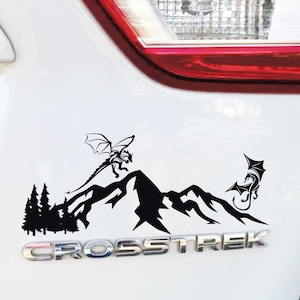 Op de afbeelding: Zwarte vinyl sticker met een bergketen met twee draken en een bos silhouet. Het woord "CROSSTREK" staat onder de afbeelding. De tekst onderaan luidt "VALDON IMAGES Unieke Aanpasbare Vinyl Decals! verschillende kleuren & maten om uit te kiezen."
