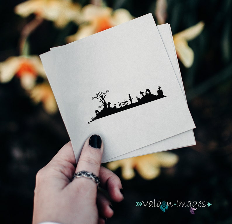May include: A black and white silhouette of a graveyard with a spooky tree, tombstones, and a fence. The image is printed on a white card.