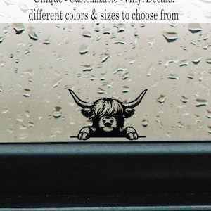 May include: Black vinyl decal of a Highland cow with large horns and shaggy fur, peeking over a line. The decal is from Valdon Images and is described as unique, customizable vinyl decals in different colors and sizes.