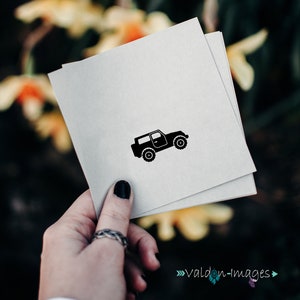 May include: A black silhouette of a jeep on a white card. The card is being held by a hand with a ring on the finger.