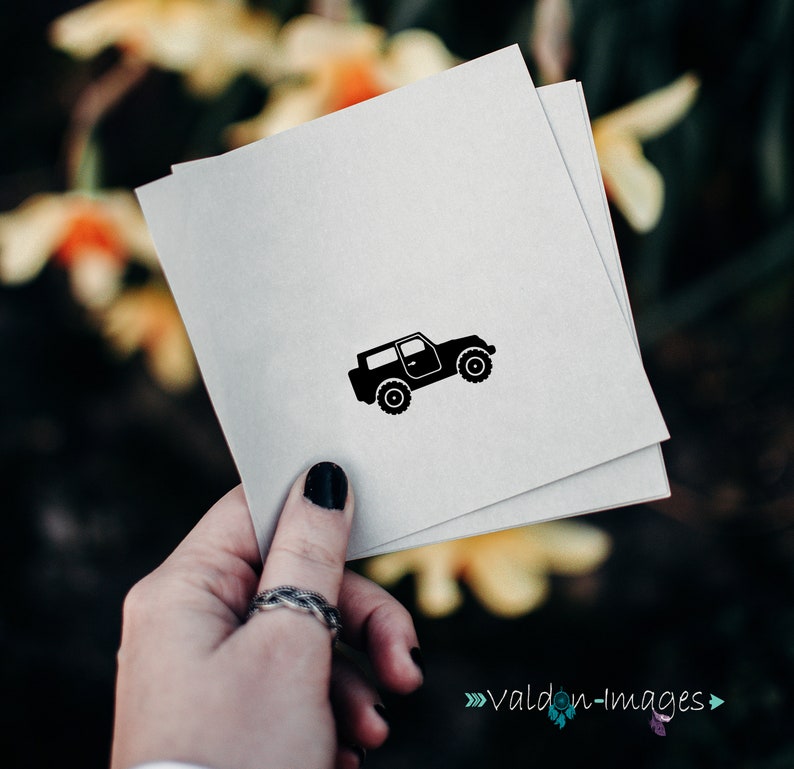 May include: A black silhouette of a jeep on a white card. The card is being held by a hand with a ring on the finger.